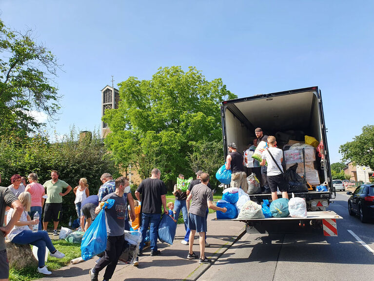 Helfer tragen Tüten und Pakete zu einem LKW